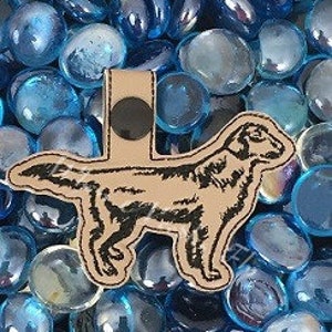 May include: A black and tan leather keychain featuring a silhouette of a golden retriever.