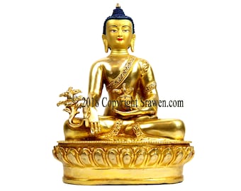 May include: A gold-coloured statue of Buddha sitting in meditation with a lotus flower in his lap. The statue is on a lotus-shaped base and has a blue crown.
