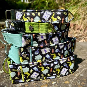 May include: A stack of dog collars with various designs. The top and bottom collars have a black background with a repeating pattern of potion bottles, candles, and other mystical symbols. The middle collars are solid green and light blue. Each collar has a metal D-ring.