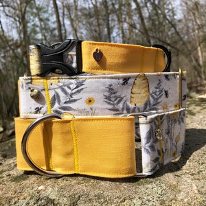 Peut inclure: Trois colliers pour chiens superposés. Le collier supérieur est jaune uni avec une boucle noire et un charm en forme de cœur. Le collier du milieu a un fond blanc avec un motif d'abeilles et de fleurs. Le collier inférieur est jaune uni avec un anneau argenté.