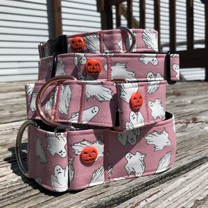 May include: A stack of three pink dog collars with a ghost and pumpkin pattern. The collars are made of fabric and have metal hardware.