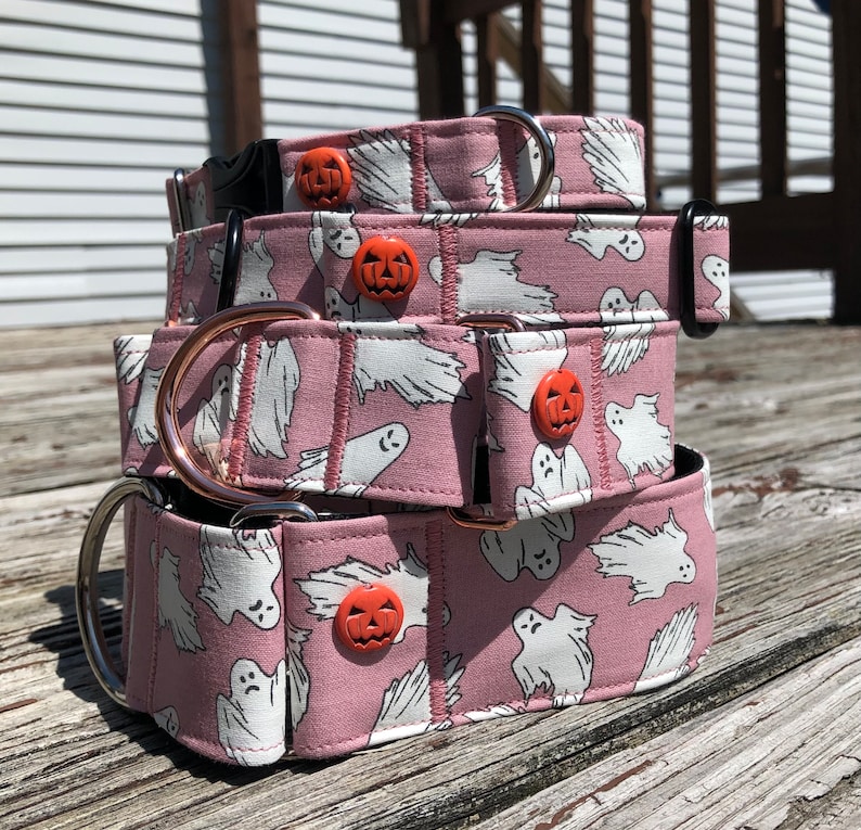 May include: A stack of three pink dog collars with a ghost and pumpkin pattern. The collars are made of fabric and have metal hardware.