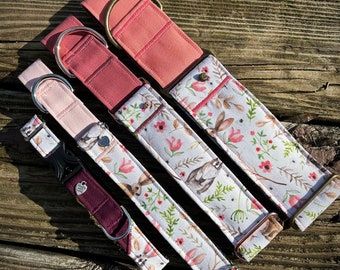May include: Four dog collars in different sizes and colors. The collars are made of fabric and have a floral pattern with a bunny rabbit design. The collars have metal hardware and are available in pink, red, and burgundy.