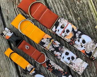 May include: Four dog collars with different patterns. The collars are made of fabric and have metal hardware. The patterns include a skull and floral design, a yellow and orange striped design, a solid orange design, and a yellow and orange striped design.