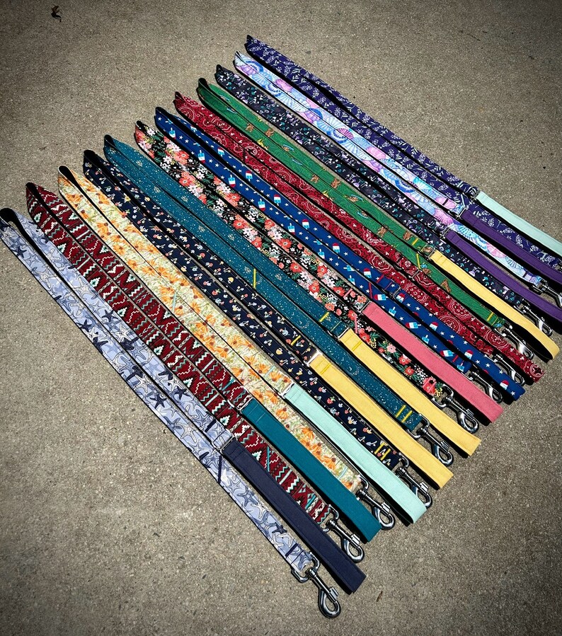May include: A collection of 20 colorful dog leashes with various patterns, including floral, geometric, and paisley designs. The leashes are arranged in a fan shape, with the ends of the leashes pointing towards the bottom of the image.