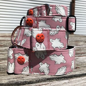May include: Three pink dog collars with a white ghost and orange pumpkin pattern. The collars are stacked on top of each other.