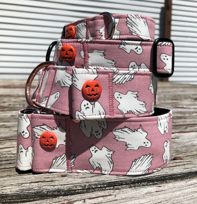 May include: Three pink dog collars with a white ghost and orange pumpkin pattern. The collars are stacked on top of each other.