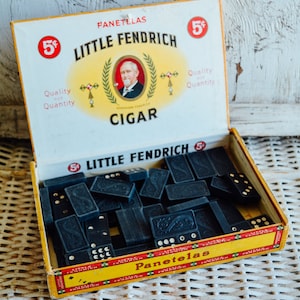 Puede incluir: Una caja abierta de dominós negros con una etiqueta amarilla y roja que dice "5¢ Little Fendrich Panetelas 5¢ Quality for Quantity Cigar".