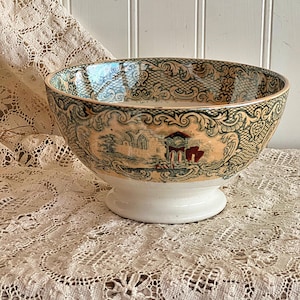 May include: A ceramic bowl featuring a pedestal base and a wide, flared rim. The exterior is decorated with a detailed transferware pattern in shades of green, tan, and red, depicting architectural ruins framed by ornate, scrolling filigree borders.