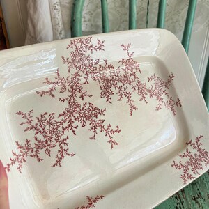 May include: Cream-coloured rectangular serving platter with a burgundy floral pattern. The pattern features delicate sprigs and floral clusters. The platter has a slightly raised edge and rounded corners, suggesting a vintage aesthetic.
