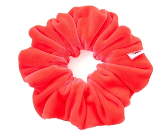 May include: A bright coral red scrunchie made of soft velvet. The scrunchie is in a gathered, bunched up style.