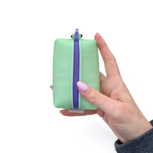 Estuche pequeño tipo caja de vinilo esmerilado verde espuma de mar con cremallera morada y llavero elástico a juego con espiral para el cabello.