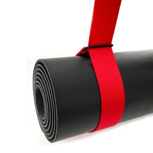 Op de afbeelding: Een zwarte yogamat die opgerold is en vastzit met een felrode band. De band heeft een metalen gesp.