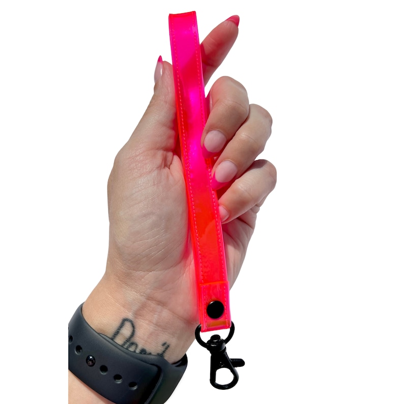 Op de afbeelding: Een felroze reflecterende sleutelhanger met een zwarte draaibare clip. De sleutelhanger is gemaakt van een helder, flexibel materiaal en heeft een reflecterend oppervlak.