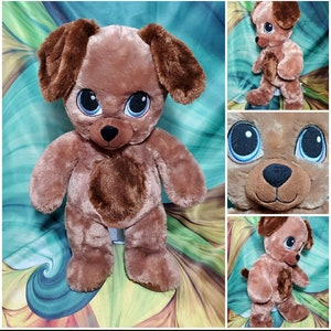 May include: A brown plush dog with big blue eyes and a brown nose. The dog is standing on a green and blue patterned surface.