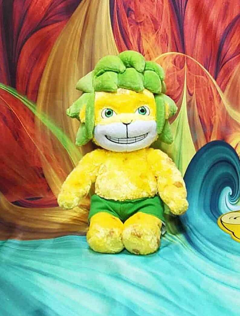 May include: A plush toy lion with a yellow body, green shorts, and a green mane. The lion has a smiling face with green eyes. The background features a colorful, abstract design with shades of red, orange, and blue.
