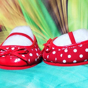 K&ouml;nnte beinhalten: Ein Paar rote Mary Jane-Schuhe mit wei&szlig;en Polka-Dots. Jeder Schuh hat einen Riemen und eine Schleife auf der Vorderseite. Die Schuhe sind mit wei&szlig;em F&uuml;llmaterial gef&uuml;llt.