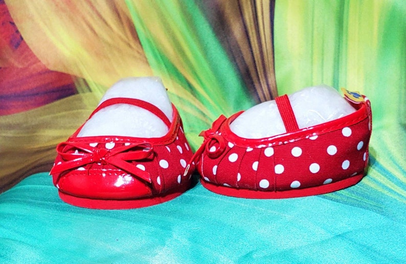 K&ouml;nnte beinhalten: Ein Paar rote Mary Jane-Schuhe mit wei&szlig;en Polka-Dots. Jeder Schuh hat einen Riemen und eine Schleife auf der Vorderseite. Die Schuhe sind mit wei&szlig;em F&uuml;llmaterial gef&uuml;llt.
