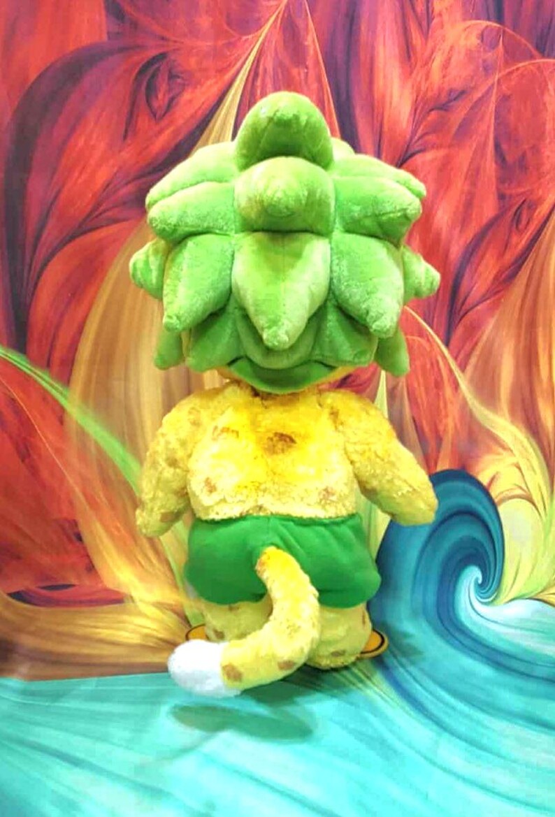 May include: A plush toy in the shape of a whimsical creature with a large, green, leafy head, yellow torso, green shorts, and a yellow tail with a white tip. The background features a colorful, abstract design with swirls of red, orange, and blue.