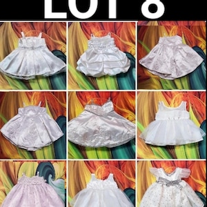 May include: Nine baby dresses in various styles and colors, including white, pink, and silver. The dresses feature details like lace, bows, and tulle. The text "LOT 8" is at the top of the image.