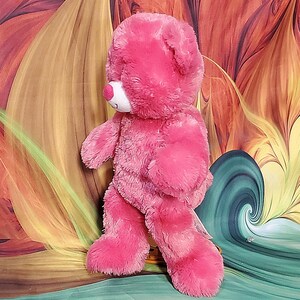 K&ouml;nnte beinhalten: Ein rosa Teddyb&auml;r mit wei&szlig;er Schnauze und rosa Nase. Der B&auml;r hat eine weiche, flauschige Textur und steht aufrecht. Das Fell des B&auml;ren ist ein leuchtender Rosaton mit dunkleren rosa Akzenten auf seinen Pfoten.