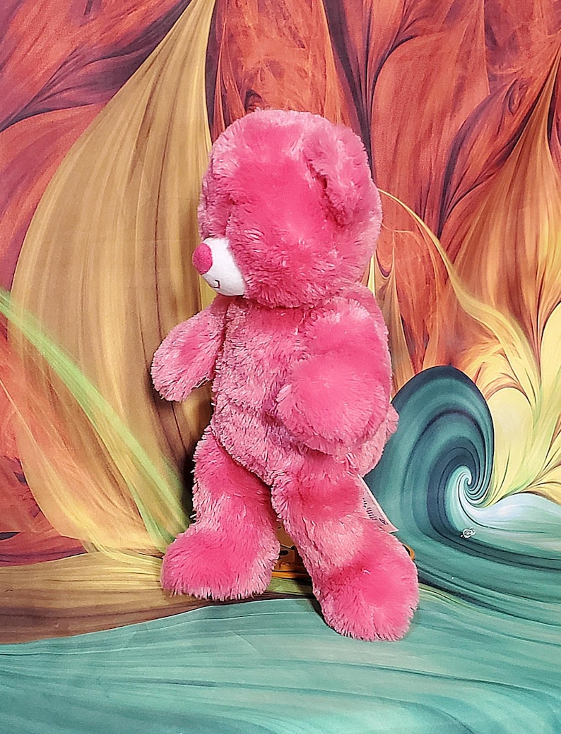 K&ouml;nnte beinhalten: Ein rosa Teddyb&auml;r mit wei&szlig;er Schnauze und rosa Nase. Der B&auml;r hat eine weiche, flauschige Textur und steht aufrecht. Das Fell des B&auml;ren ist ein leuchtender Rosaton mit dunkleren rosa Akzenten auf seinen Pfoten.