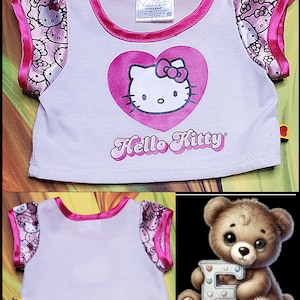 Może przedstawiać: Biała koszulka Hello Kitty z r&oacute;żowymi wykończeniami i rękawami. Koszulka posiada duże r&oacute;żowe serce z twarzą Hello Kitty i napisem "Hello Kitty" w kursywie. Rękawy mają wz&oacute;r Hello Kitty.