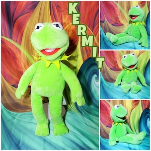 May include: A bright green plush frog toy with large white eyes, a wide mouth with a red interior, and a yellow collar. The plush features long limbs and a soft texture. The word KERMIT is printed in green capital letters vertically on the right side.