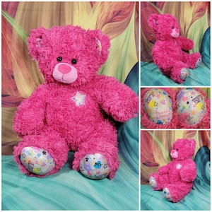 May include: A vibrant pink plush teddy bear with a star on its chest and colorful paw pads. The bear has a pink nose and black eyes. The paw pads feature the text "BFF" and "Friends Count".
