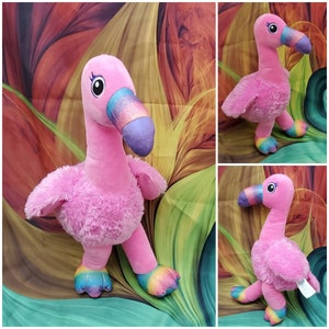 May include: Pink plush flamingo toy with rainbow accents on the beak and feet. The flamingo is standing on a colorful background.