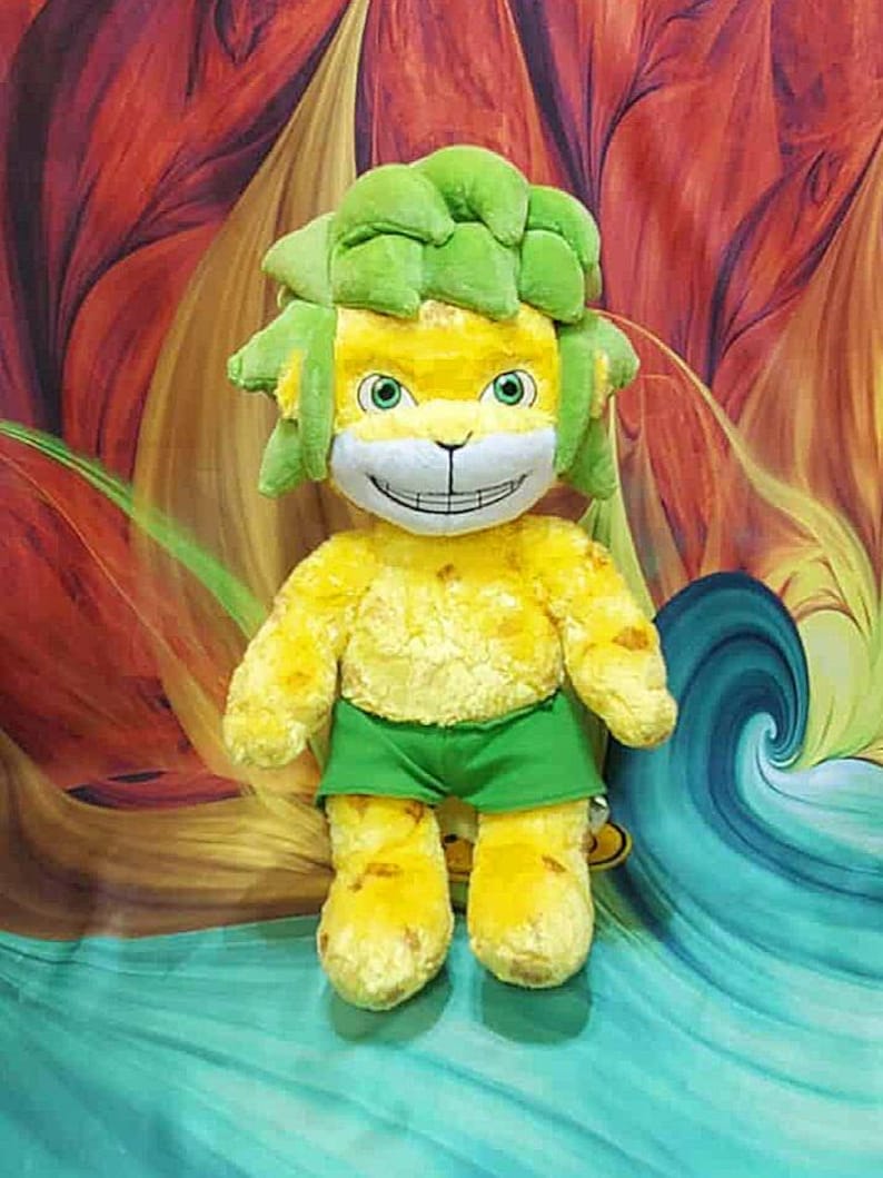 May include: A plush toy lion with a yellow body, green hair, and green shorts. The lion has a smiling face with green eyes. The background is a colorful abstract design.