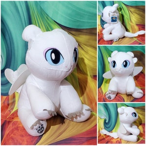 May include: White plush dragon toy with large blue eyes, small wings, and a long tail. The dragon has a friendly expression and is sitting. The dragon has the letters "B-A-B" on its paw.