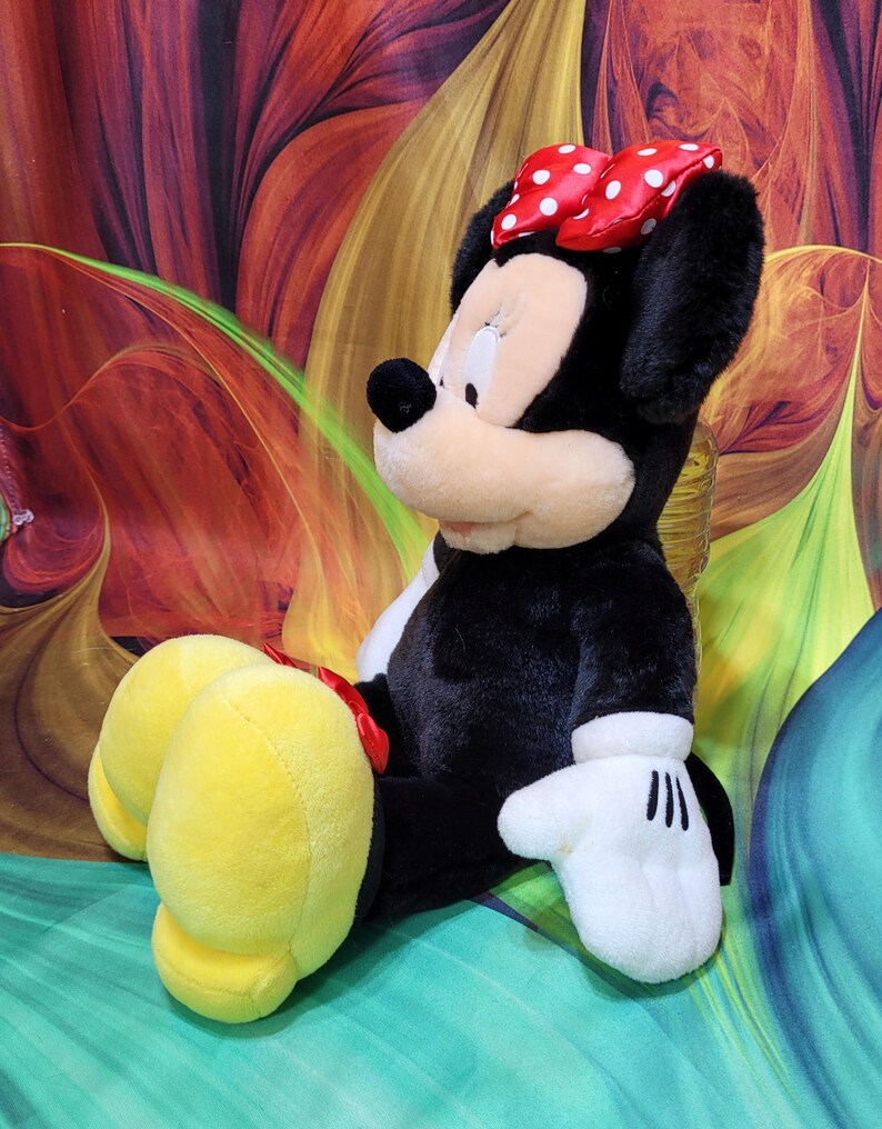 K&ouml;nnte beinhalten: Eine Pl&uuml;schpuppe von Minnie Mouse mit schwarzem Fell, einem wei&szlig;en Gesicht und gro&szlig;en gelben F&uuml;&szlig;en. Sie tr&auml;gt eine rote Schleife mit wei&szlig;en Punkten und wei&szlig;e Handschuhe. Ein klassischer Disney-Charakter.