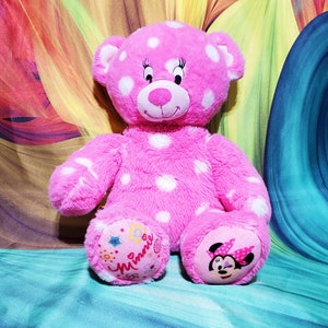 May include: Pink polka dot plush teddy bear with a Minnie Mouse face on one foot and the word "Minnie" on the other foot.