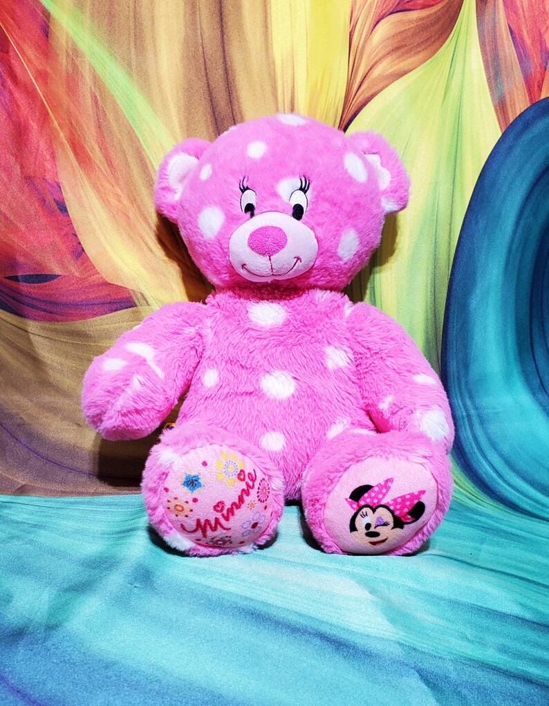 May include: Pink polka dot plush teddy bear with a Minnie Mouse face on one foot and the word "Minnie" on the other foot.