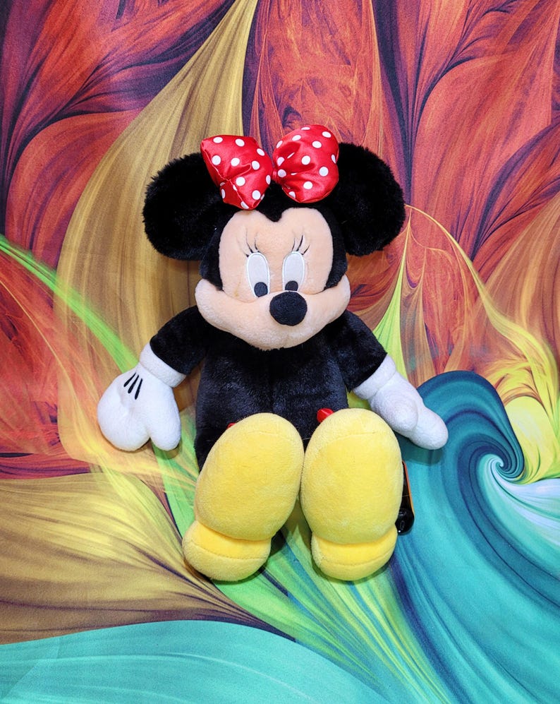 K&ouml;nnte beinhalten: Eine Pl&uuml;schpuppe von Minnie Mouse, mit einem schwarzen K&ouml;rper, gro&szlig;en schwarzen Ohren und einer roten Schleife mit wei&szlig;en Punkten. Die Puppe hat wei&szlig;e Handschuhe und gelbe Schuhe. Der Hintergrund ist ein farbenfrohes abstraktes Design.