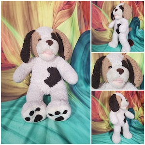 May include: A plush brown and white dog with a brown patch on its chest. The dog is sitting on a colorful patterned fabric.
