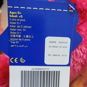 Puede incluir: Una etiqueta azul con texto en varios idiomas, incluyendo "Ages 0+" y "SS MINNIE MS BEAR." La etiqueta est&aacute; adjunta a un peluche rosa y esponjoso. La etiqueta tambi&eacute;n incluye un c&oacute;digo de barras y el n&uacute;mero "0229560012177."