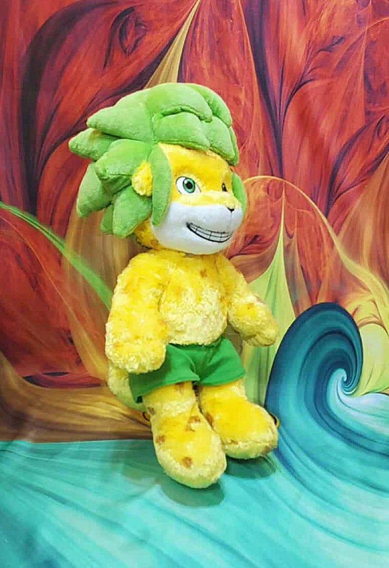 May include: A plush toy lion with a yellow body, green hair, and green shorts. The lion has a smiling face with white fur and green eyes. The background features a colorful, abstract design with red, orange, and blue hues.