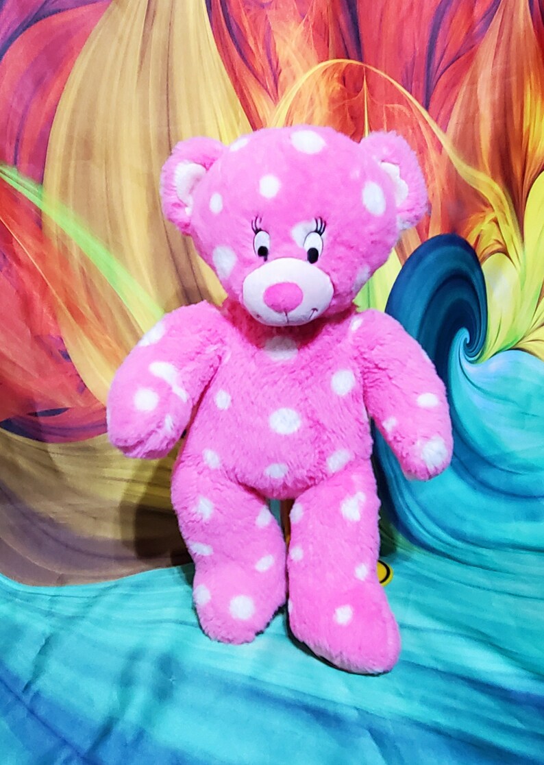 May include: Pink plush teddy bear with white polka dots. The bear has a pink nose and black eyes with eyelashes.