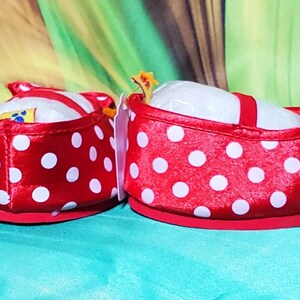 K&ouml;nnte beinhalten: Ein Paar rote Babyschuhe mit wei&szlig;en Tupfen. Die Schuhe haben einen roten Riemen und eine Schleife. Die Schuhe sind mit wei&szlig;er Polsterung gef&uuml;llt. Die Schuhe sind f&uuml;r Babys konzipiert.