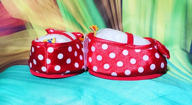 K&ouml;nnte beinhalten: Ein Paar rote Babyschuhe mit wei&szlig;en Tupfen. Die Schuhe haben einen roten Riemen und eine Schleife. Die Schuhe sind mit wei&szlig;er Polsterung gef&uuml;llt. Die Schuhe sind f&uuml;r Babys konzipiert.