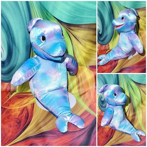 May include: A plush blue and purple dolphin toy with a shimmery finish. The dolphin has a large, open mouth and a friendly expression.