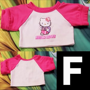 Może przedstawiać: Biała i r&oacute;żowa koszulka w stylu raglan z grafiką Hello Kitty. Koszulka ma r&oacute;żowy dekolt i rękawy, z postacią Hello Kitty i napisem "Hello Kitty" wydrukowanym z przodu.