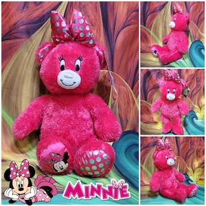 Puede incluir: Un oso de peluche rosa brillante con un dise&ntilde;o de Minnie Mouse. El oso tiene un gran lazo con lunares plateados, un hocico blanco y un gr&aacute;fico de Minnie Mouse en su pie. La palabra "Minnie" se muestra en texto rosa.