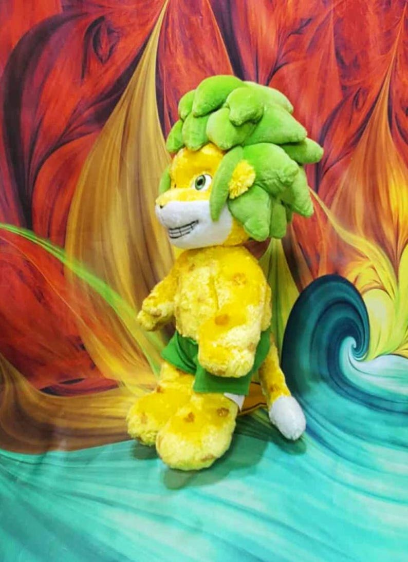 May include: A plush toy lion with a yellow body and green mane and shorts. The lion has a smiling face with white teeth and paws. The background is a colorful abstract design with swirls of red, orange, and blue.