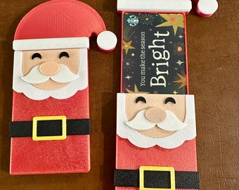 Puede incluir: Dos tarjeteros rojos con temática de Papá Noel. Uno cerrado y otro abierto, mostrando una tarjeta de regalo con "Bright" y "You make the season". Tienen ribetes blancos y cinturones negros. Tema navideño festivo.