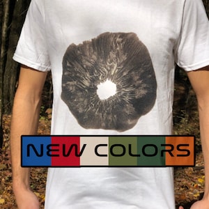 Puede incluir: Camiseta blanca con un gráfico de hongo en blanco y negro y el texto "NEW COLORS" en azul, rojo, beige, verde y naranja.