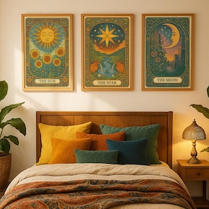 以下が含まれることがあります： 「太陽」、「星」、「月」の3枚のタロットカードのフレームプリント。それぞれ、ヴィンテージスタイルで詳細なイラストが描かれており、暖色系の色と装飾的なボーダーが特徴です。カラフルな枕と模様入りのスローが置かれたベッドの上に飾られています。