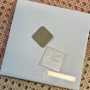 May include: Two rubber stamps, one brown and one clear, with a design of a turnip with leaves. The stamps are on a white surface.